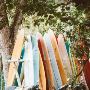A vibrant display of colorful surfboards stacked next to parked motorcycles under lush tree canopy.